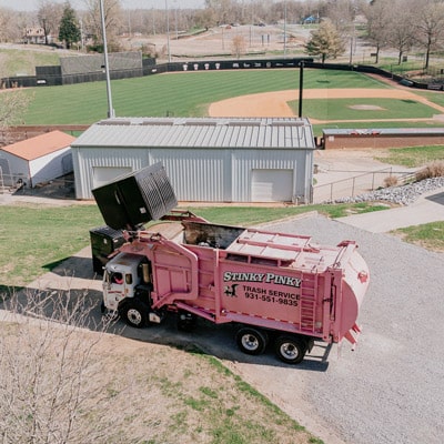 Commercial Dumpster being picked up by Commercial Garbage truck at a baseball field