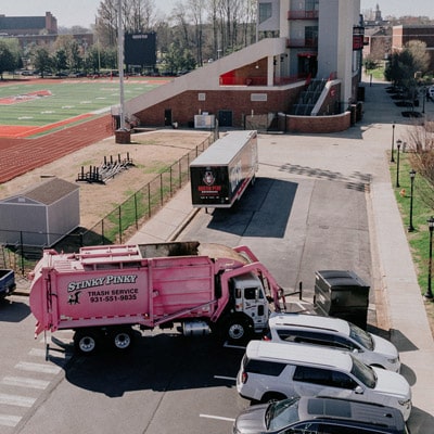 Commercial Dumpster being picked up by Commercial Garbage truck at a football field